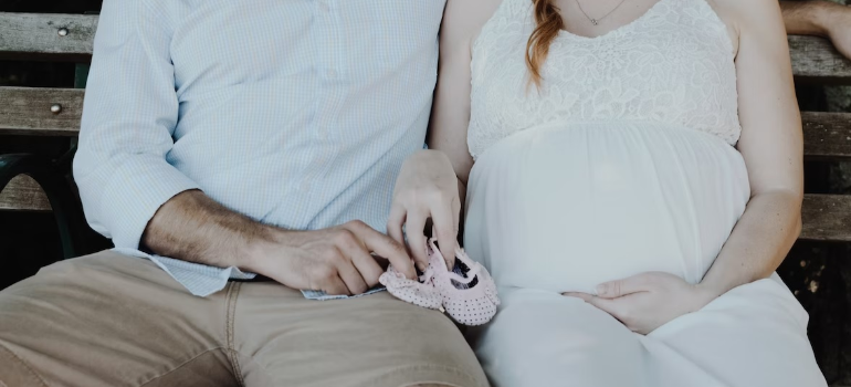 A pregnant woman and her husband holding baby shoes.